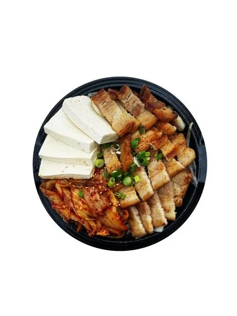 A bowl of Korean fried chicken with slices of tofu, chopped green onions, and kimchi.