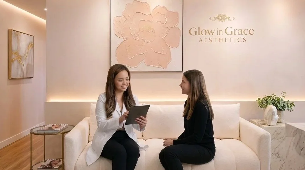 A consultation in a wellness or aesthetic clinic, with a professional woman showing a tablet to a patient. The background has a sign that reads 'Glow in Grace Aesthetics' and floral artwork.