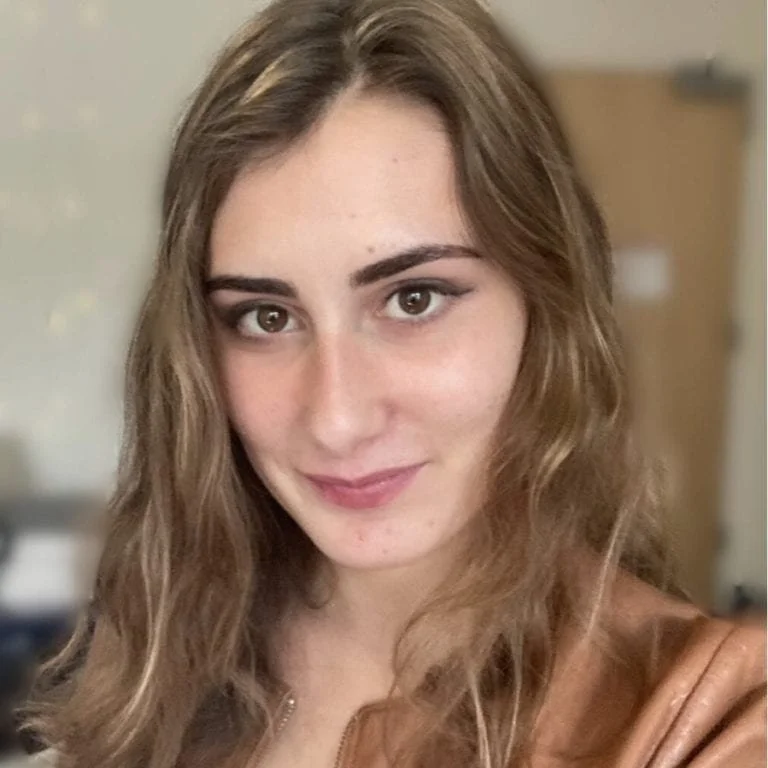 A young woman with long, wavy light-brown hair, fair skin, and brown eyes smiling at the camera.