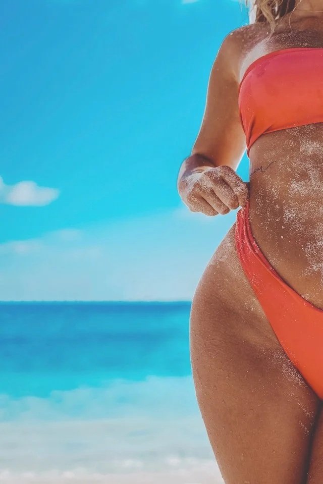 A woman in her swim wear on the beach with a tan.