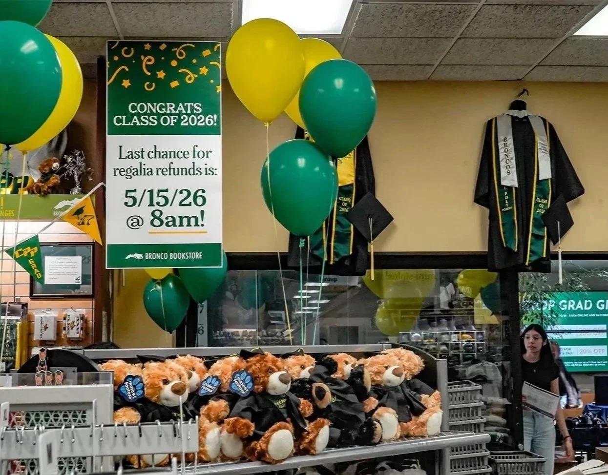 Graduation decorations in a bookstore, including green and yellow balloons, stuffed animals wearing graduation caps, and a sign with graduation date details.