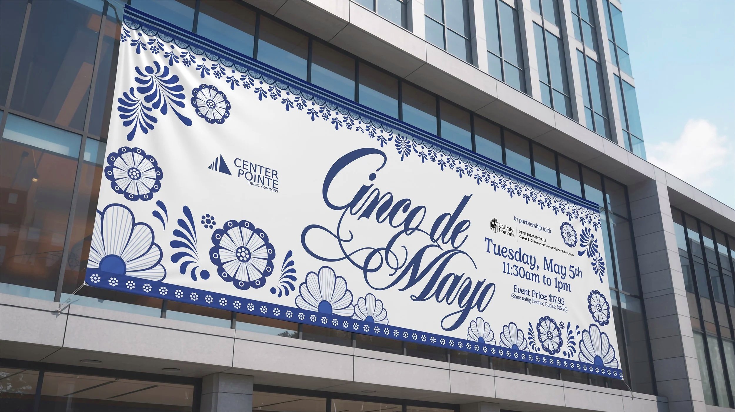 Large banner hanging outside a modern building advertising the Cinco de Mayo celebration on Tuesday, May 5th from 11:30 am to 1 pm, organized by Center Pointe dining commons and Cal Poly Pomona, featuring decorative blue floral patterns.