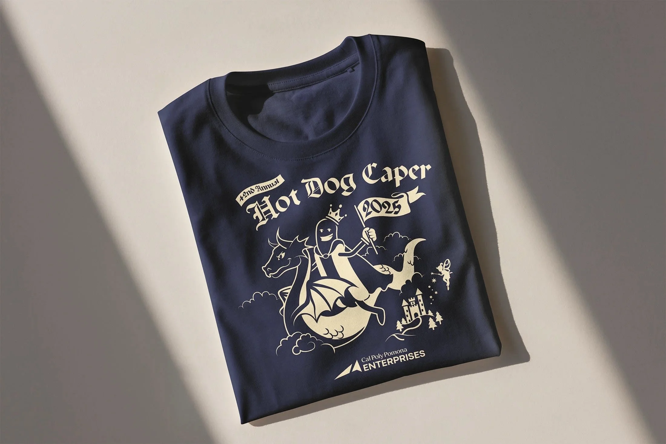 A navy blue T-shirt with white print celebrating Cal Poly Pomona's 75th Annual Hot Dog Caper event, featuring a dragon cartoon mascot and the logo of Cal Poly Pomona Enterprises.