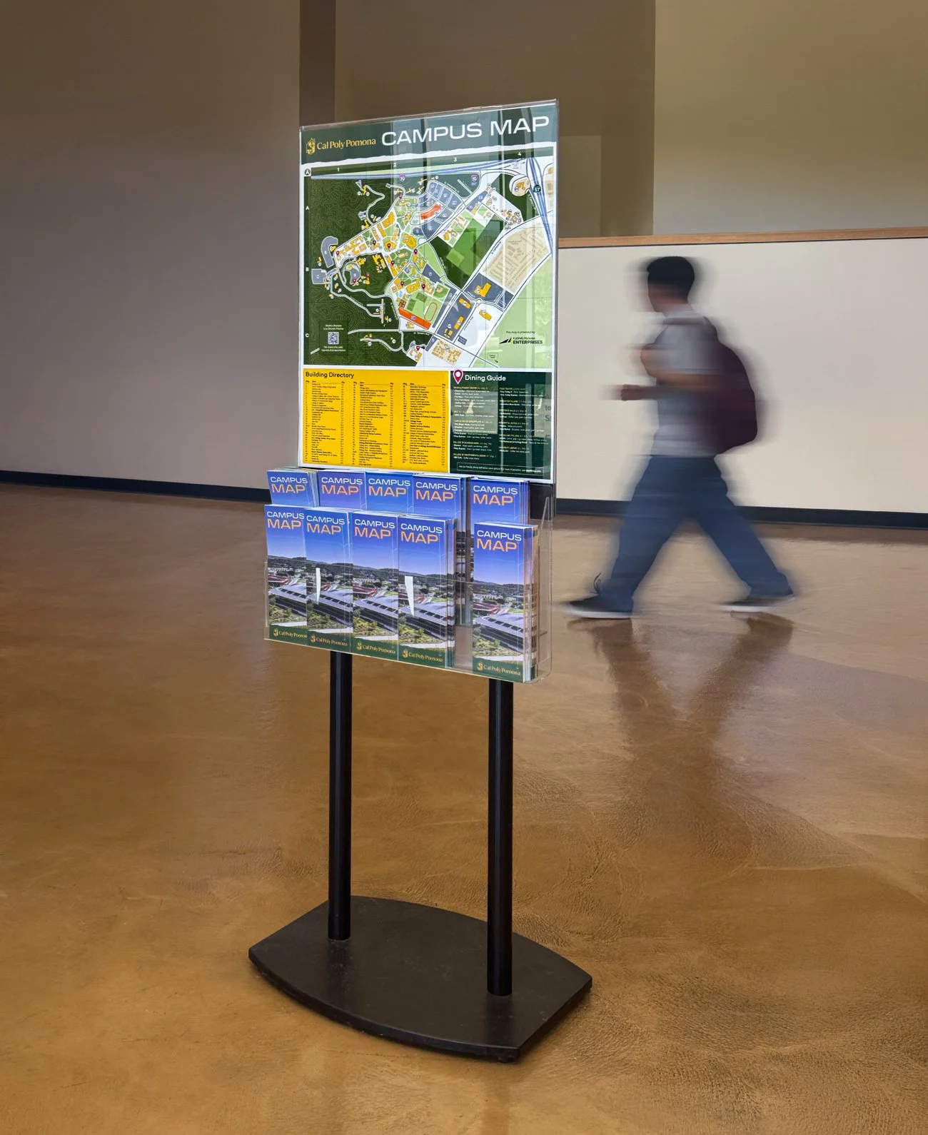 Campus map display at Cal Poly Pomona with brochures and guide, and a person walking by in the background.