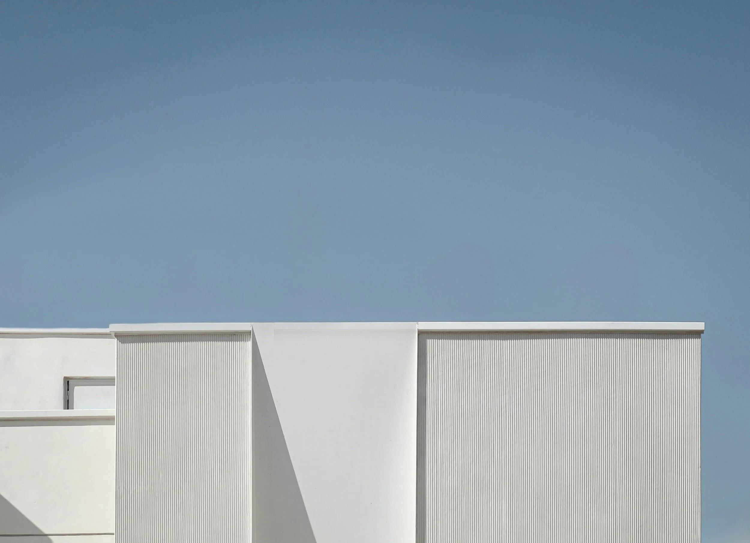 A modern white building with vertical lines on its facade and a clear blue sky above.