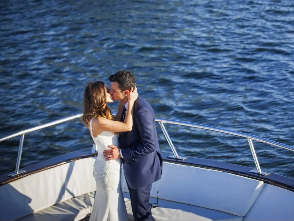 A newly married couple embracing and sharing a kiss on MV Pearl with water in the background.