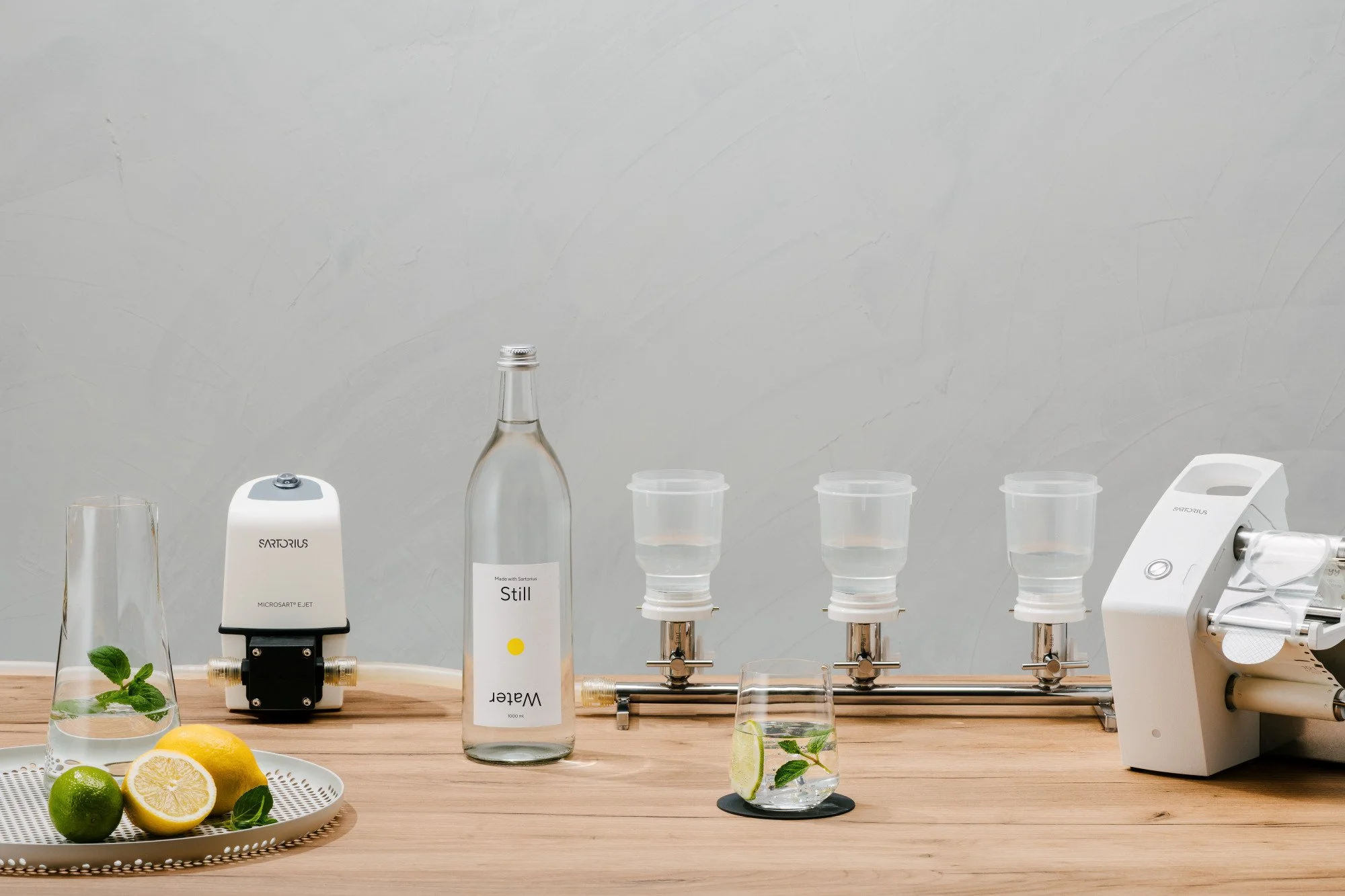 Instrumentos y vasos con agua, limón y menta en una mesa de laboratorio, con un fondo de pared gris.