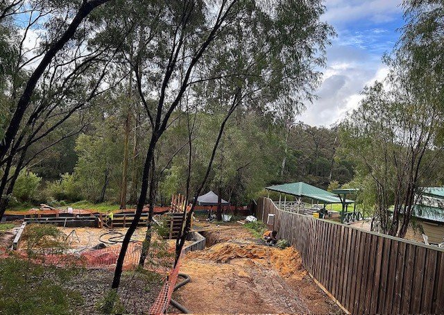 A backyard under construction with a wooden fence, trees, and construction equipment.