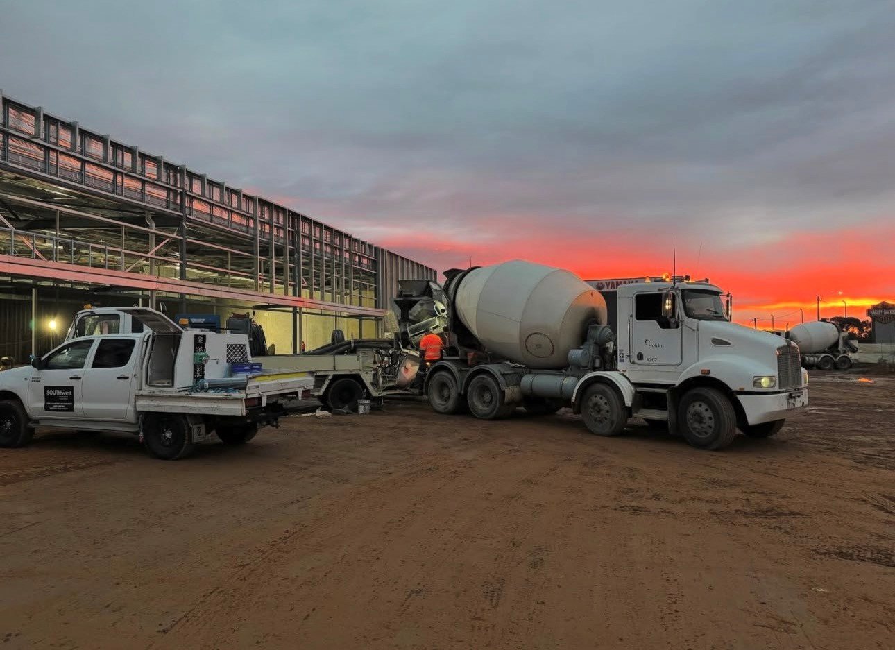 Construction site at sunset with cement mixer trucks and construction worker.