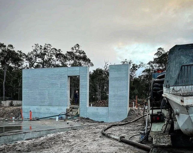 Construction site with a concrete structure, a humorous cut-out doorway, and construction equipment, with a forested background.