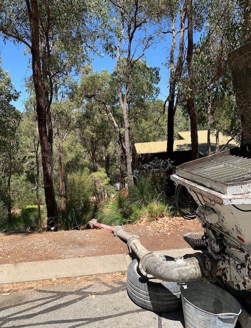 Part of a boat's engine and exhaust pipe on a paved street, with trees and houses in the background.
