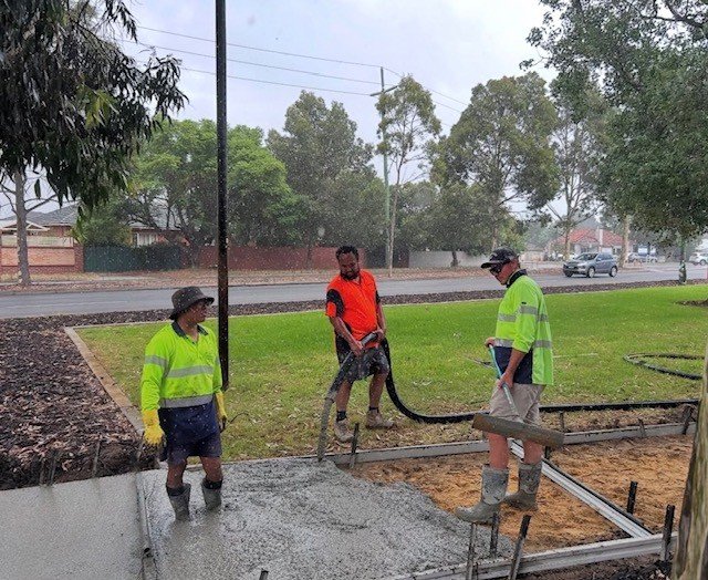 Three construction workers in high-visibility clothing working on concrete pouring at a construction site outdoors.