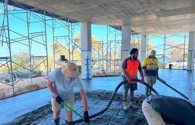 Construction workers pouring and spreading concrete on a building's floor.