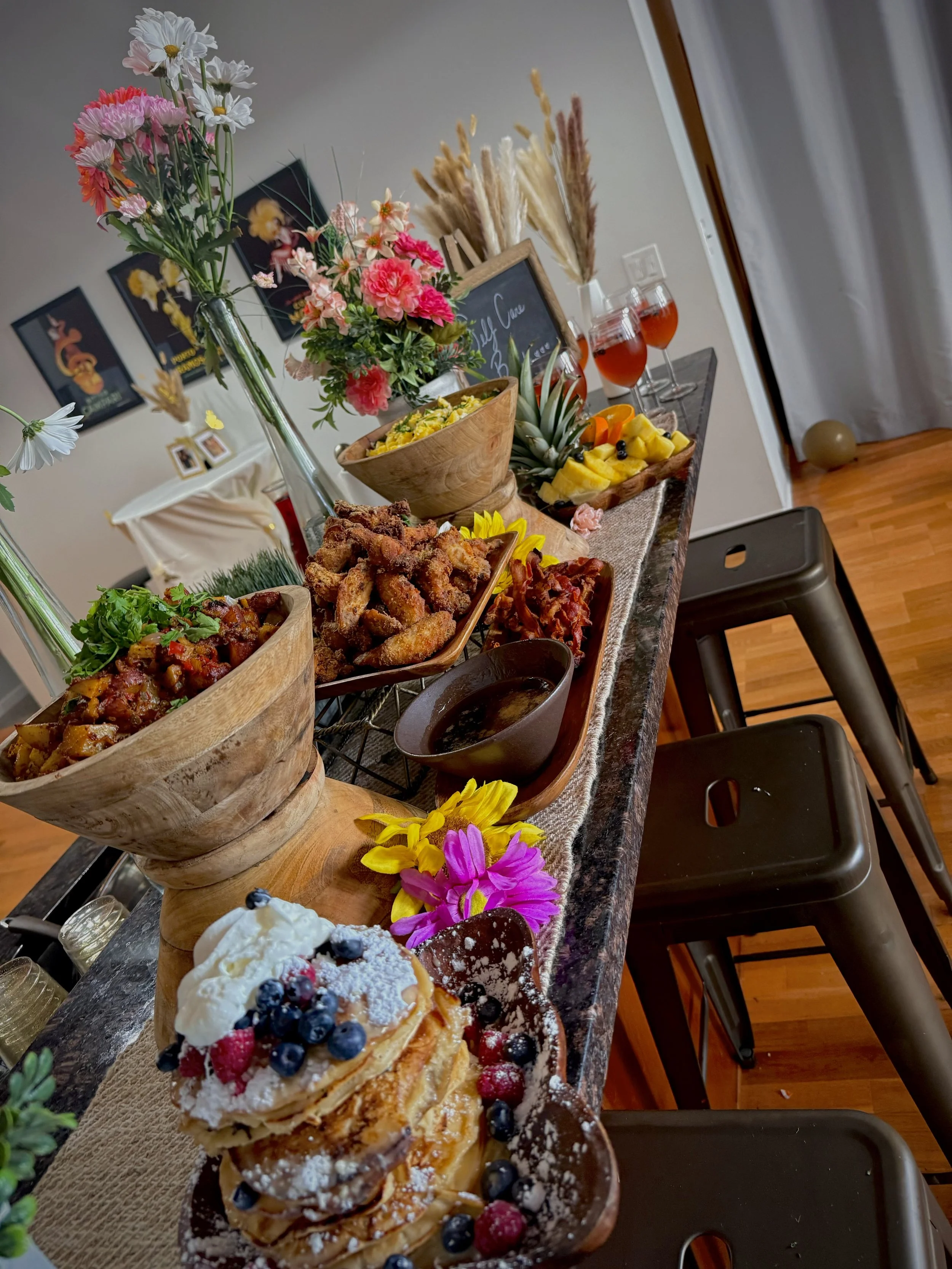 A table decorated with flowers and an assortment of desserts, including layered pastry with berries, fruit salad, fried chicken, and drinks.