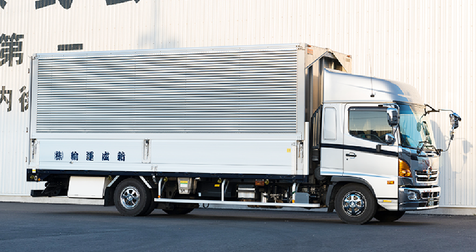 白いトラックが並んだ貨物車両。建物の側に停車している。