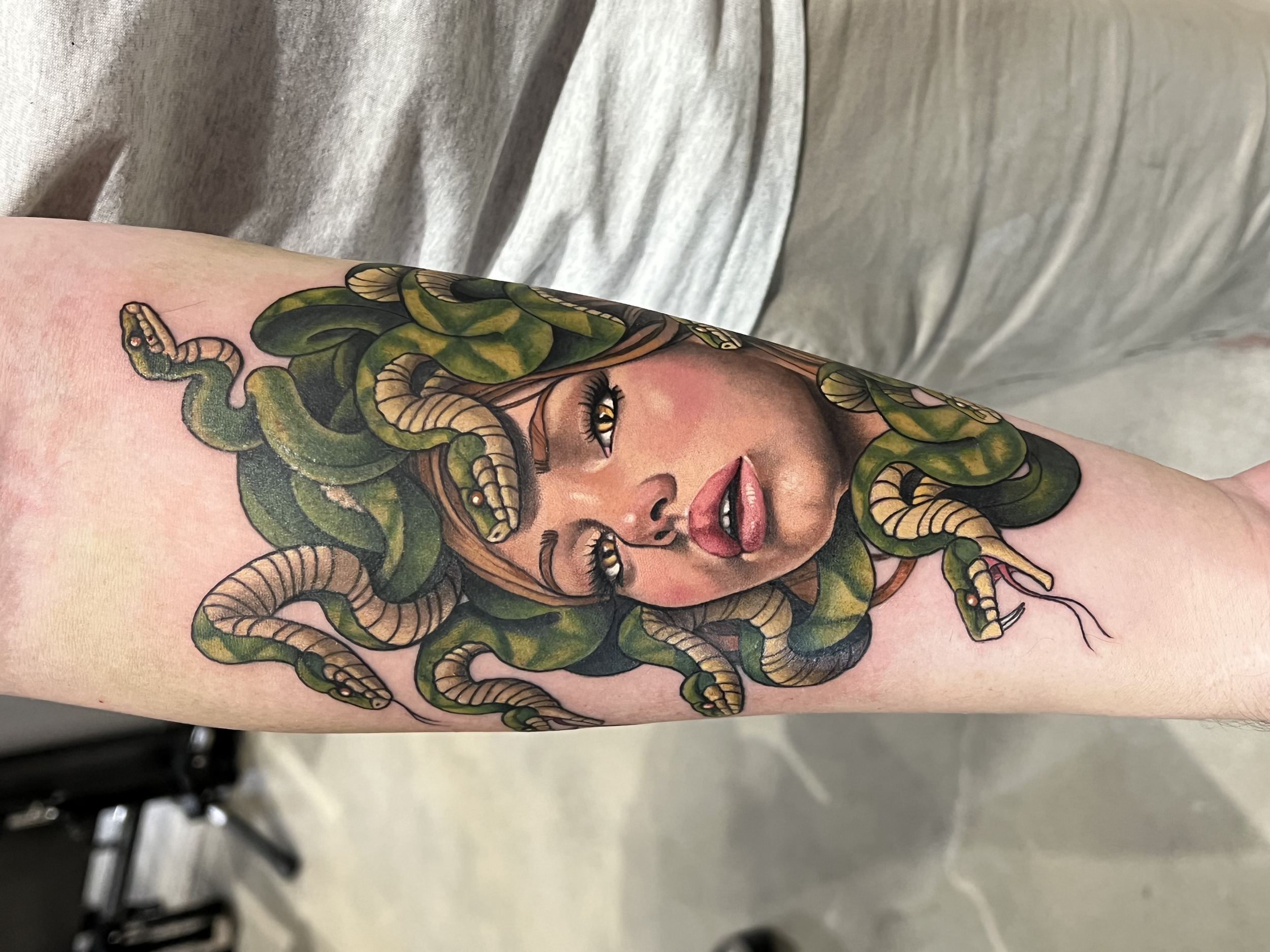 A colorful tattoo of a woman with foliage and snakes on her face and back, with a background of a gray fabric surface.