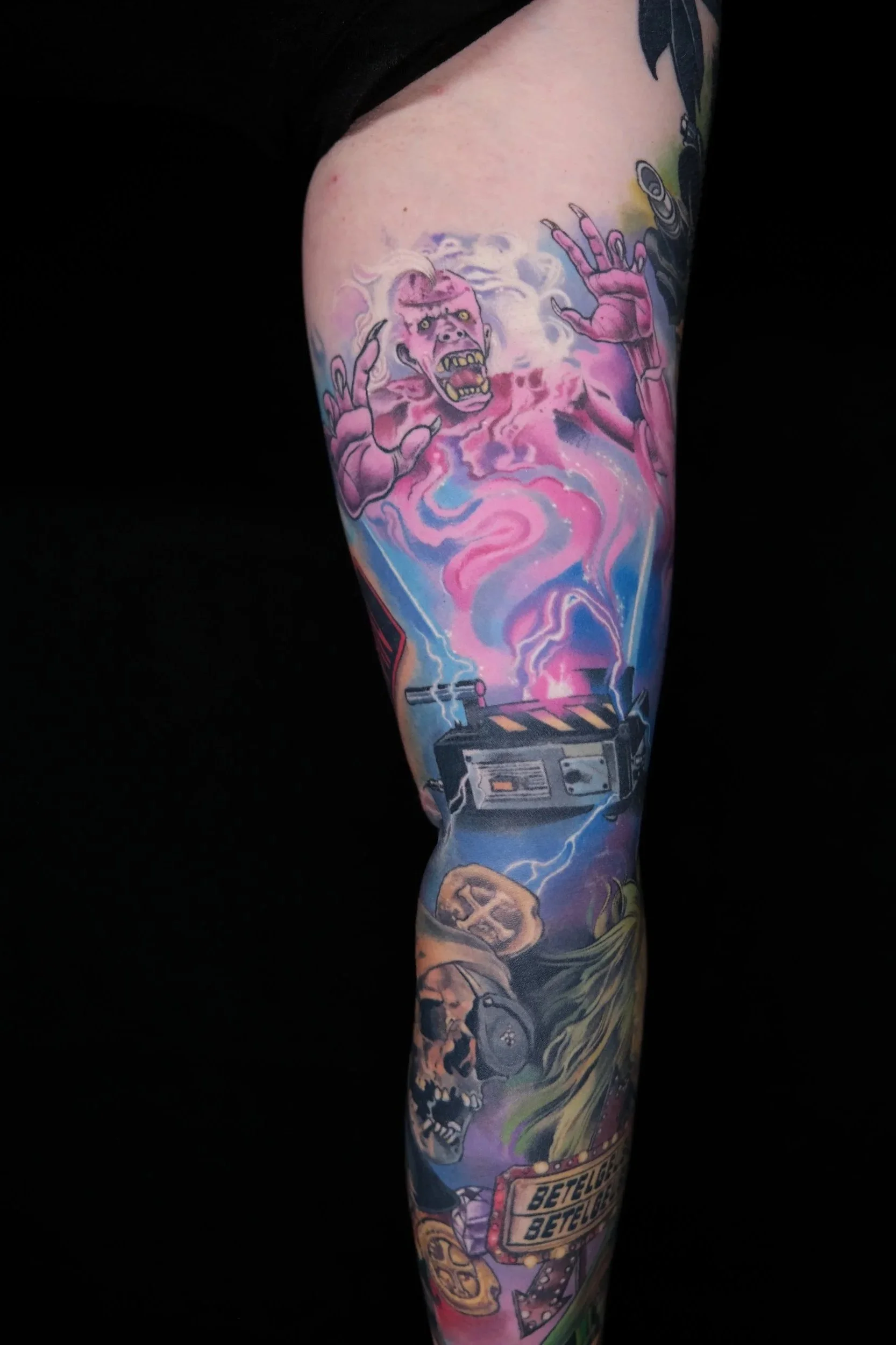 A colorful tattoo sleeve featuring a pink zombie-like creature with glowing eyes and sharp teeth, surrounded by abstract cosmic and mechanical elements, including a box labeled 'BETELGEUSE' and cosmic clouds.
