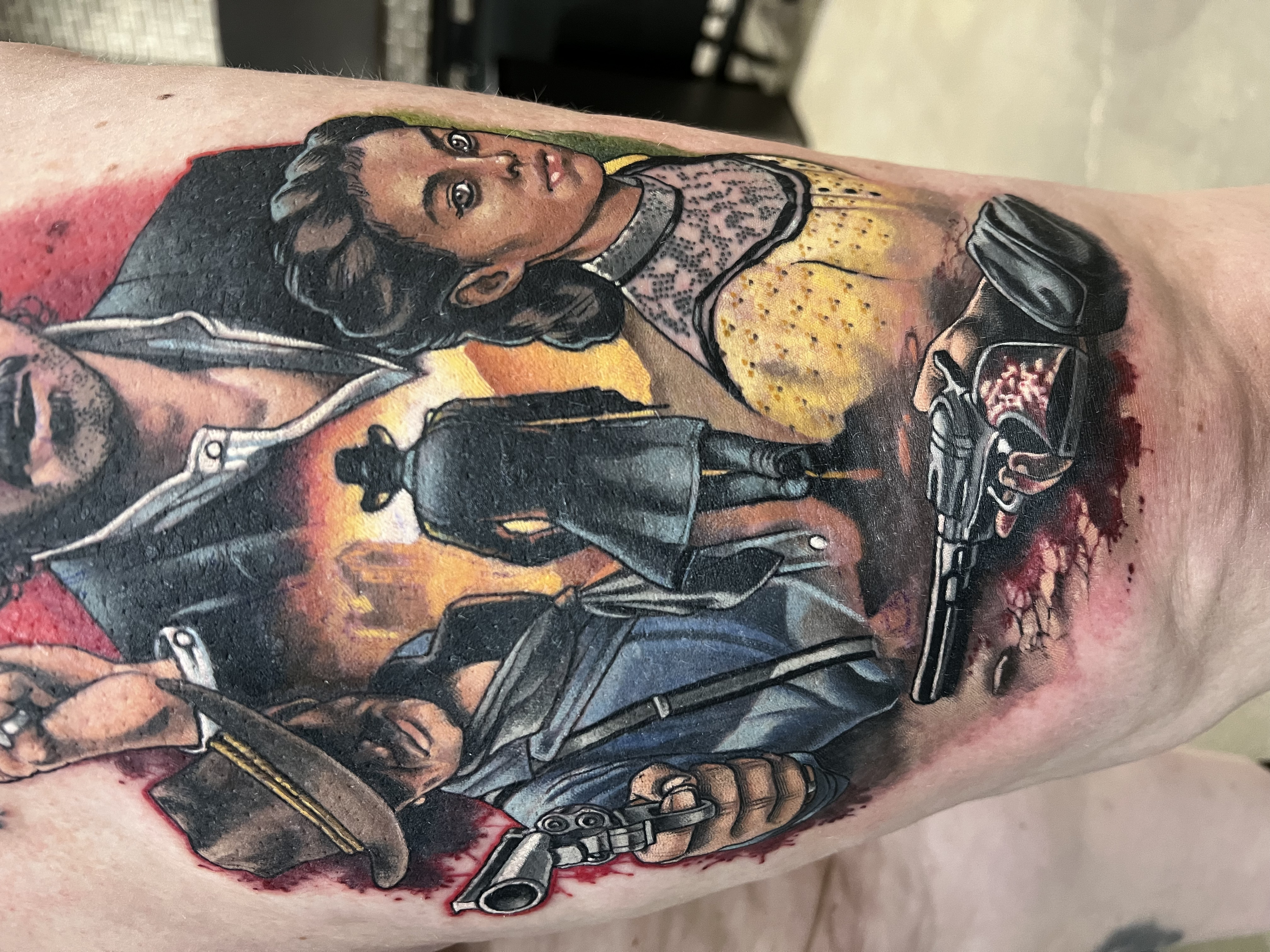 A realistic tattoo of a woman with dark hair and brown skin, dressed in armor, holding a futuristic weapon, with a background of orange and yellow hues.