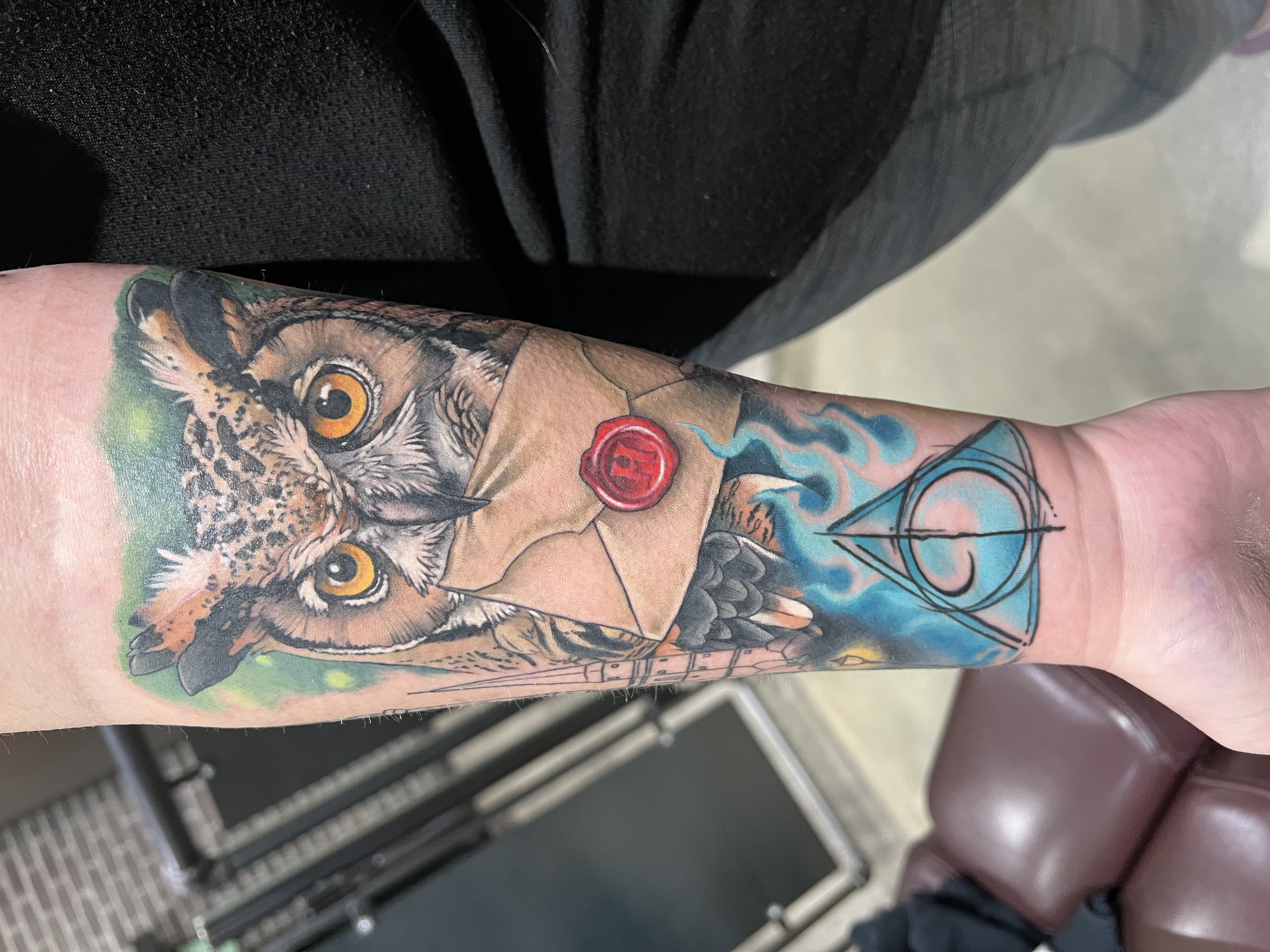 Colorful tattoo on a person's forearm depicting an animal, possibly a cat or a wolf, with orange eyes and detailed fur, surrounded by colorful flames or energy patterns.