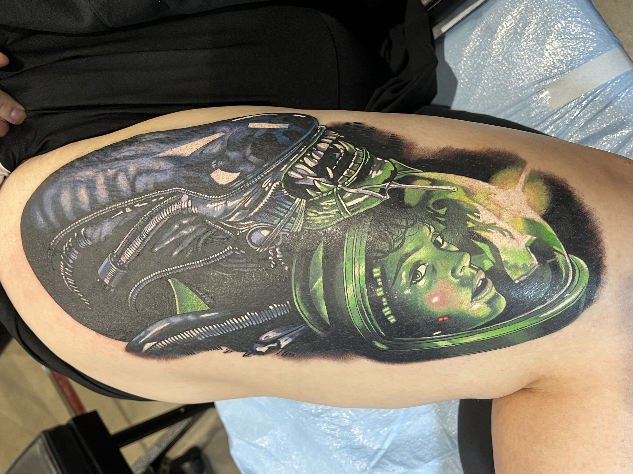 Color upper thigh tattoo of a Xenomorph along with a green hued portrait of Ripley