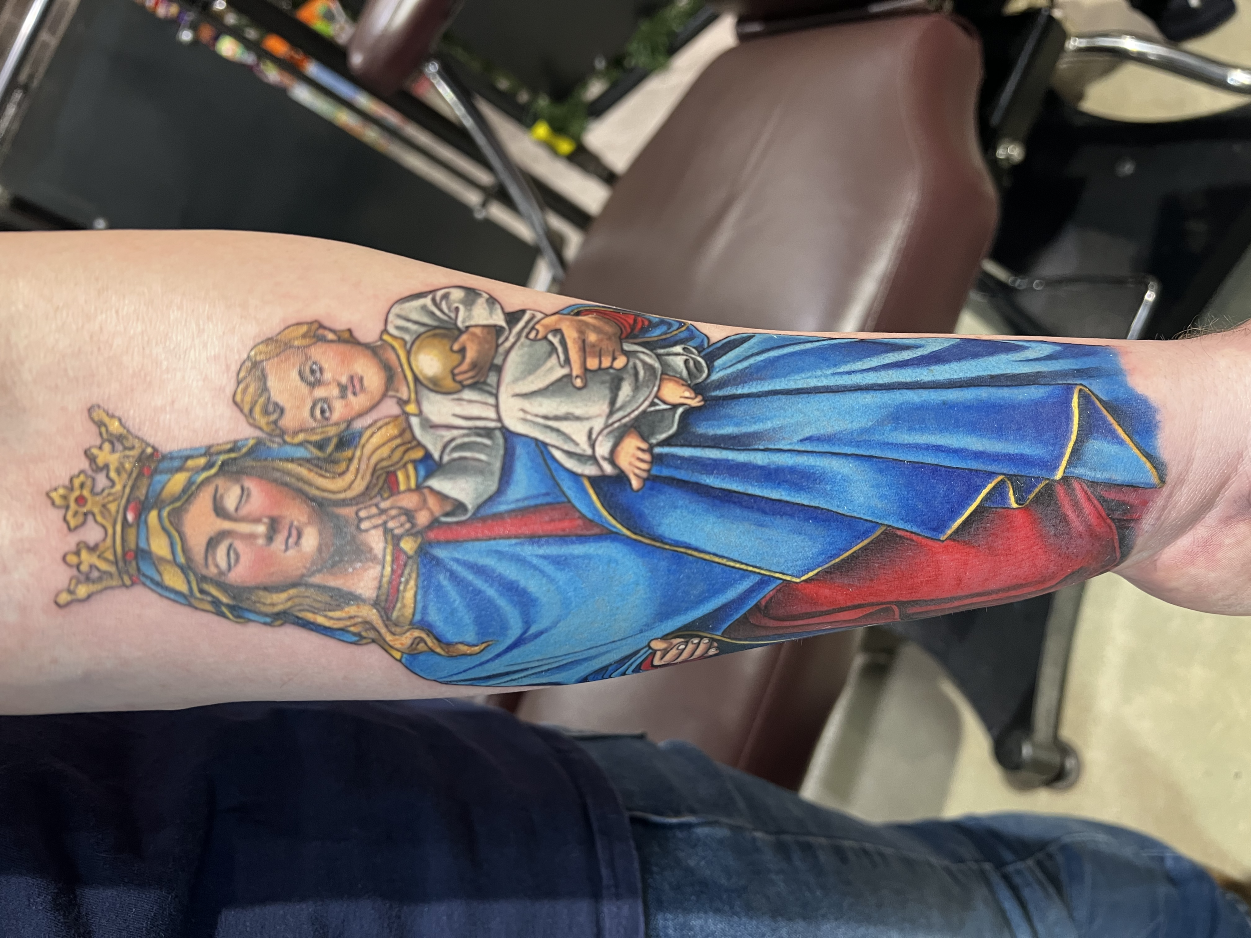 Tattoo of the Virgin Mary holding baby Jesus on person's arm.
