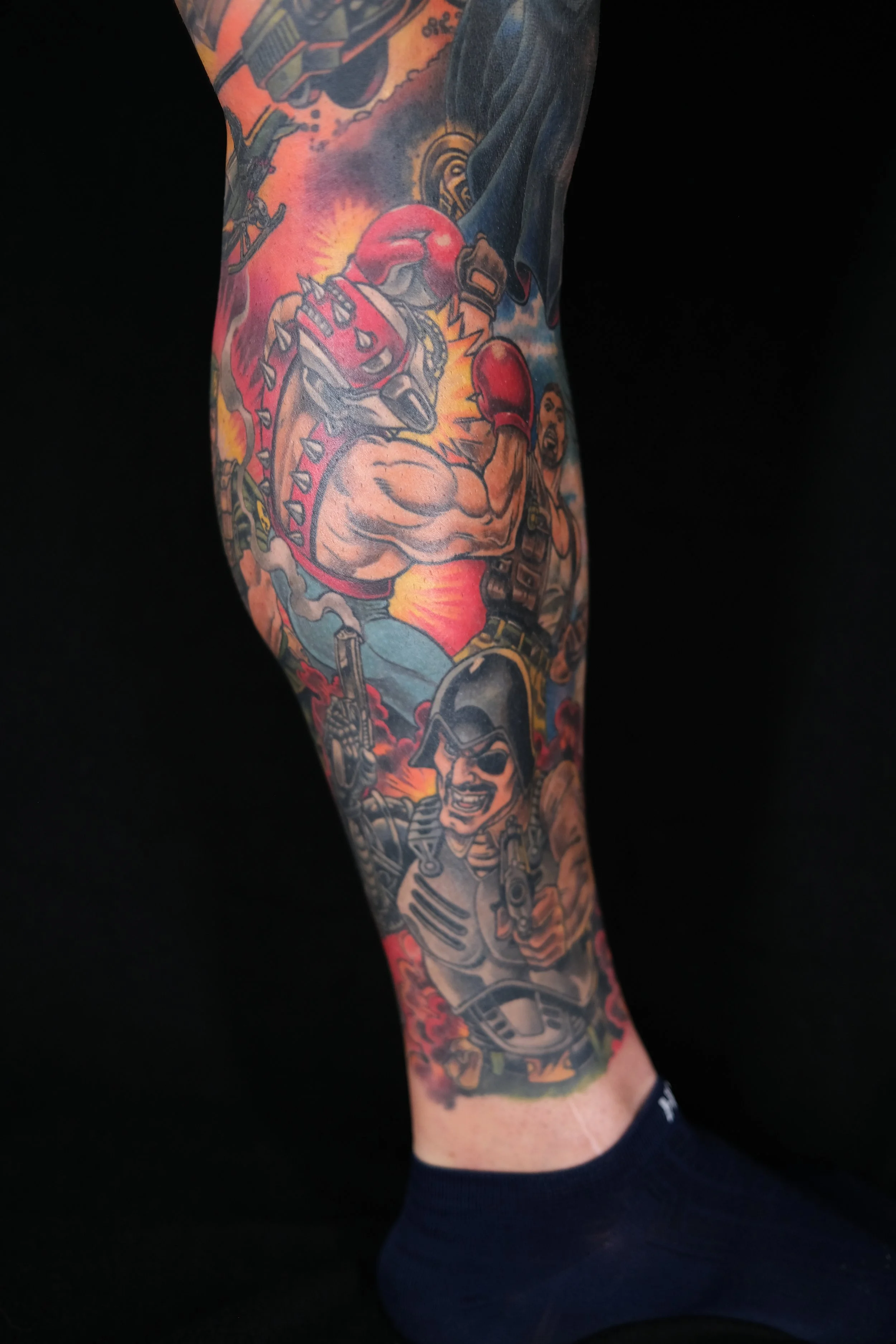 Colorful tattoo sleeve on a person's arm, featuring a boxing scene with a boxer wearing red gloves and shorts, surrounded by vibrant flames and dynamic background elements.