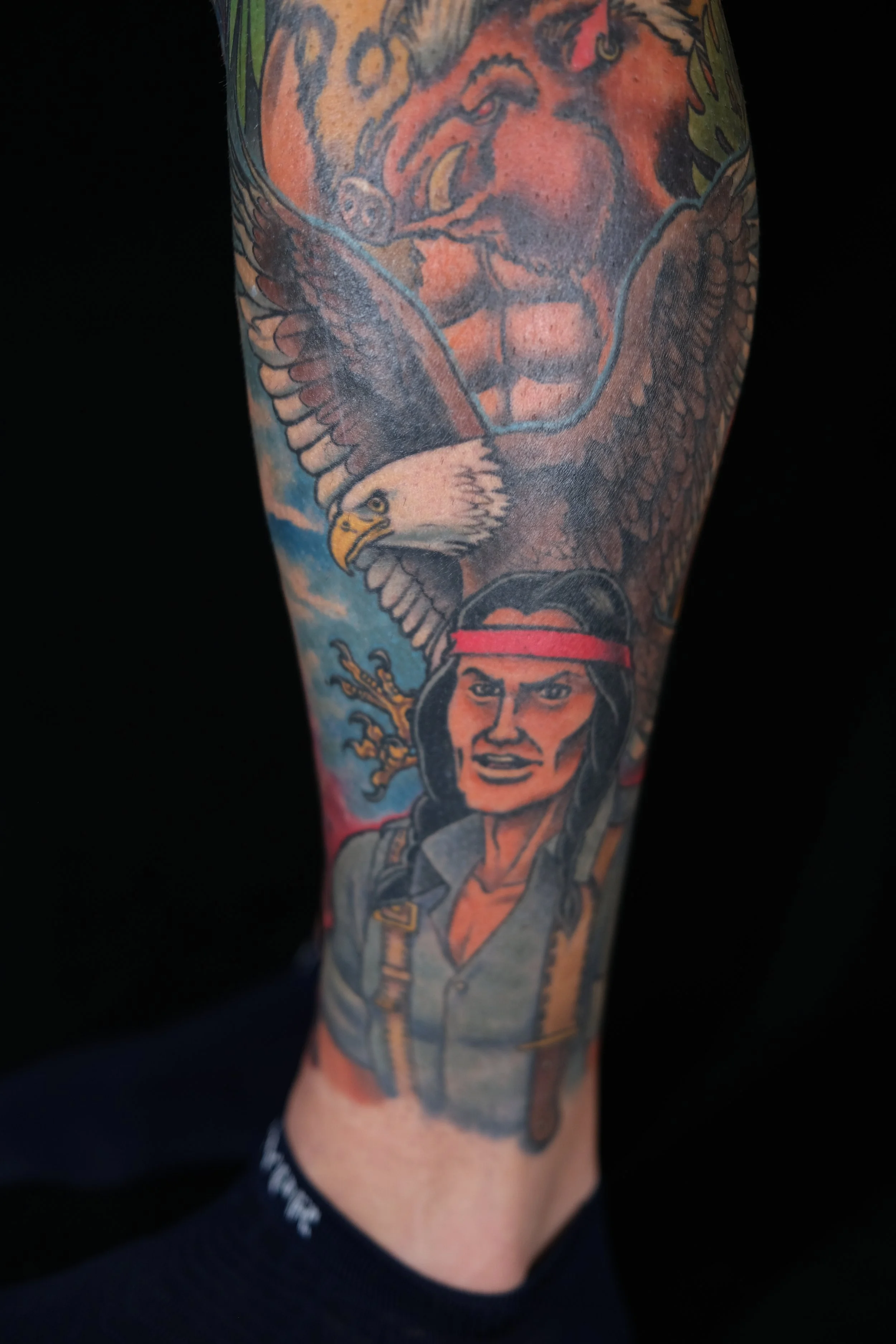 Colorful tattoo sleeve featuring an eagle, a woman's face, and other elements on a person's arm.