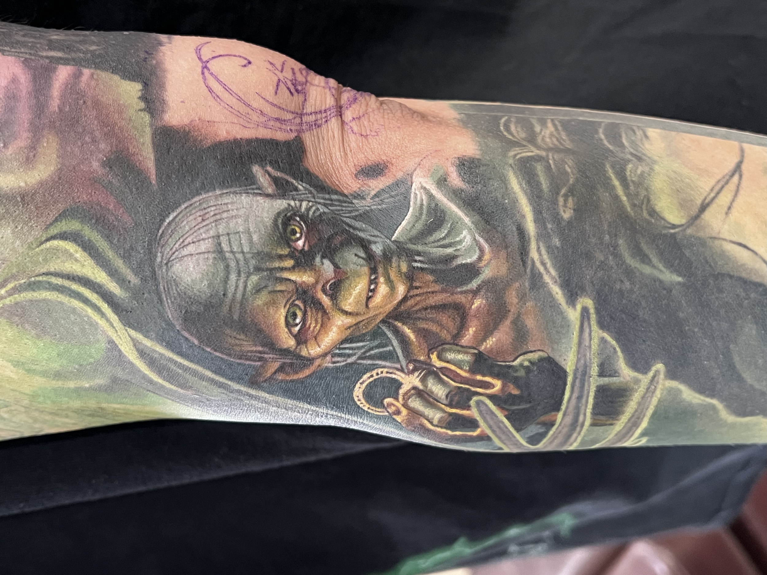 Close-up of a tattooed person's skin with detailed artwork of a woman's face, including dark hair, reminiscent of a painting or graphic novel style.