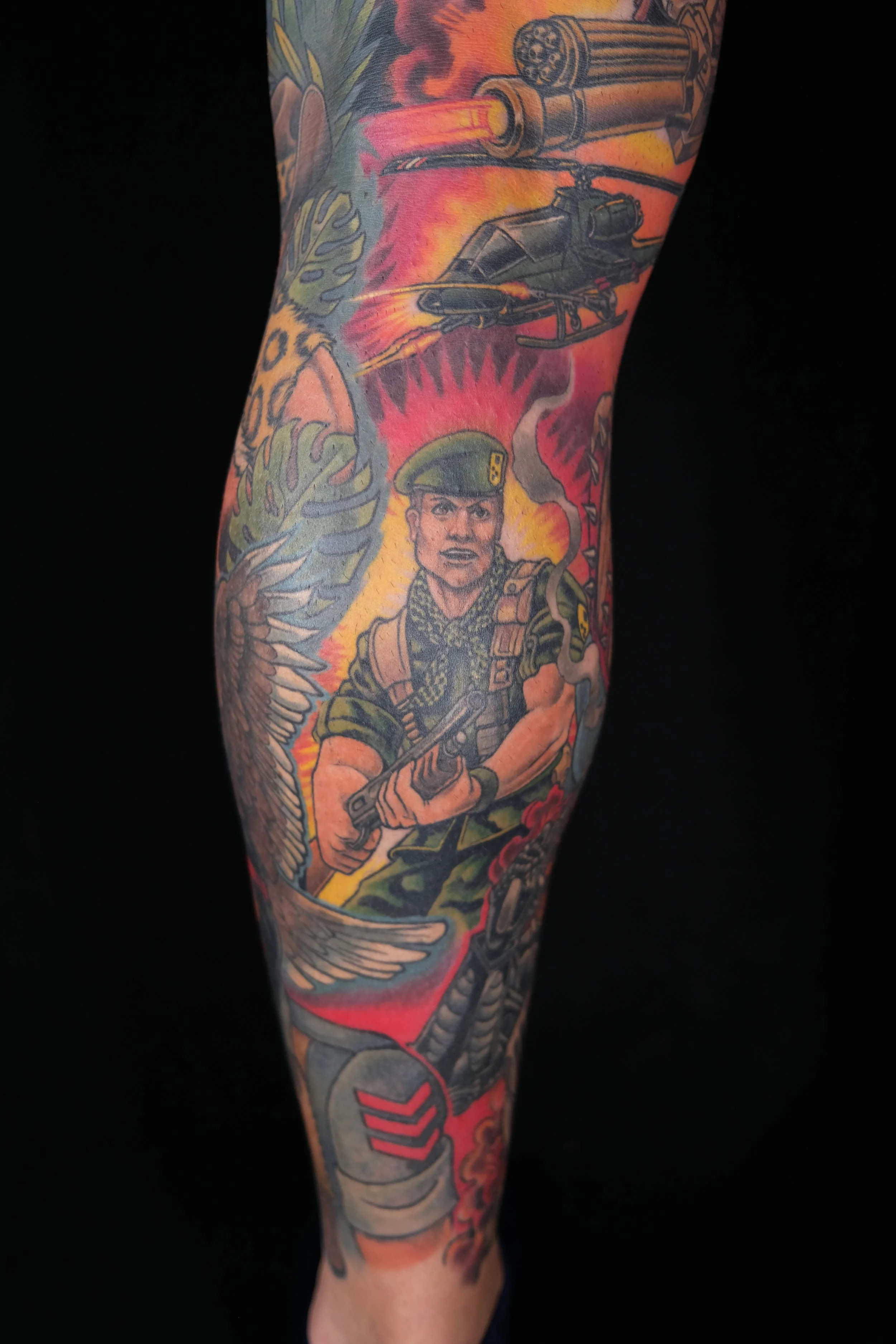 A tattoo sleeve on a person's arm depicting military and combat imagery, including a soldier, helicopter, gunfire, missile, and military insignia.