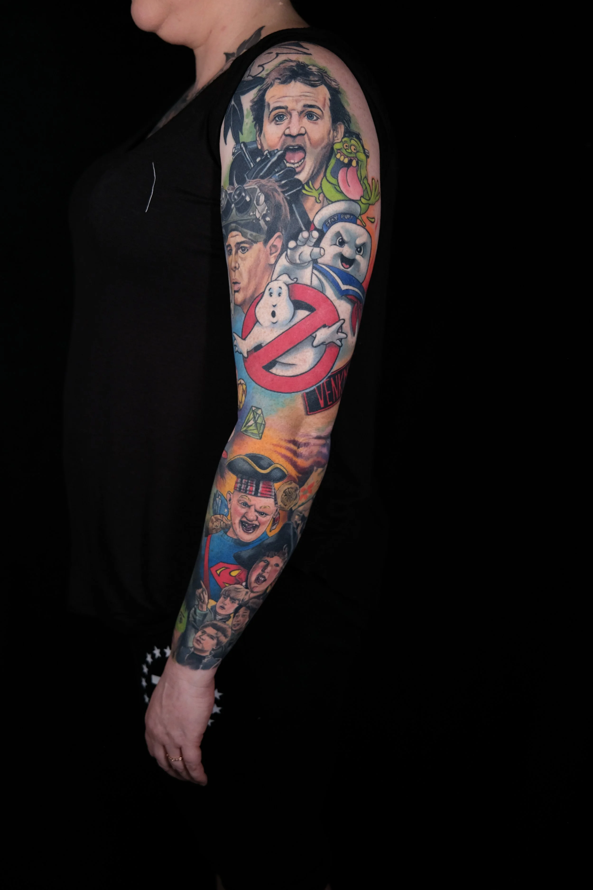 Close-up of a tattooed arm featuring various pop culture characters including a man with a surprised expression, a cartoon ghost, a green monster with its tongue out, and other animated faces and symbols.