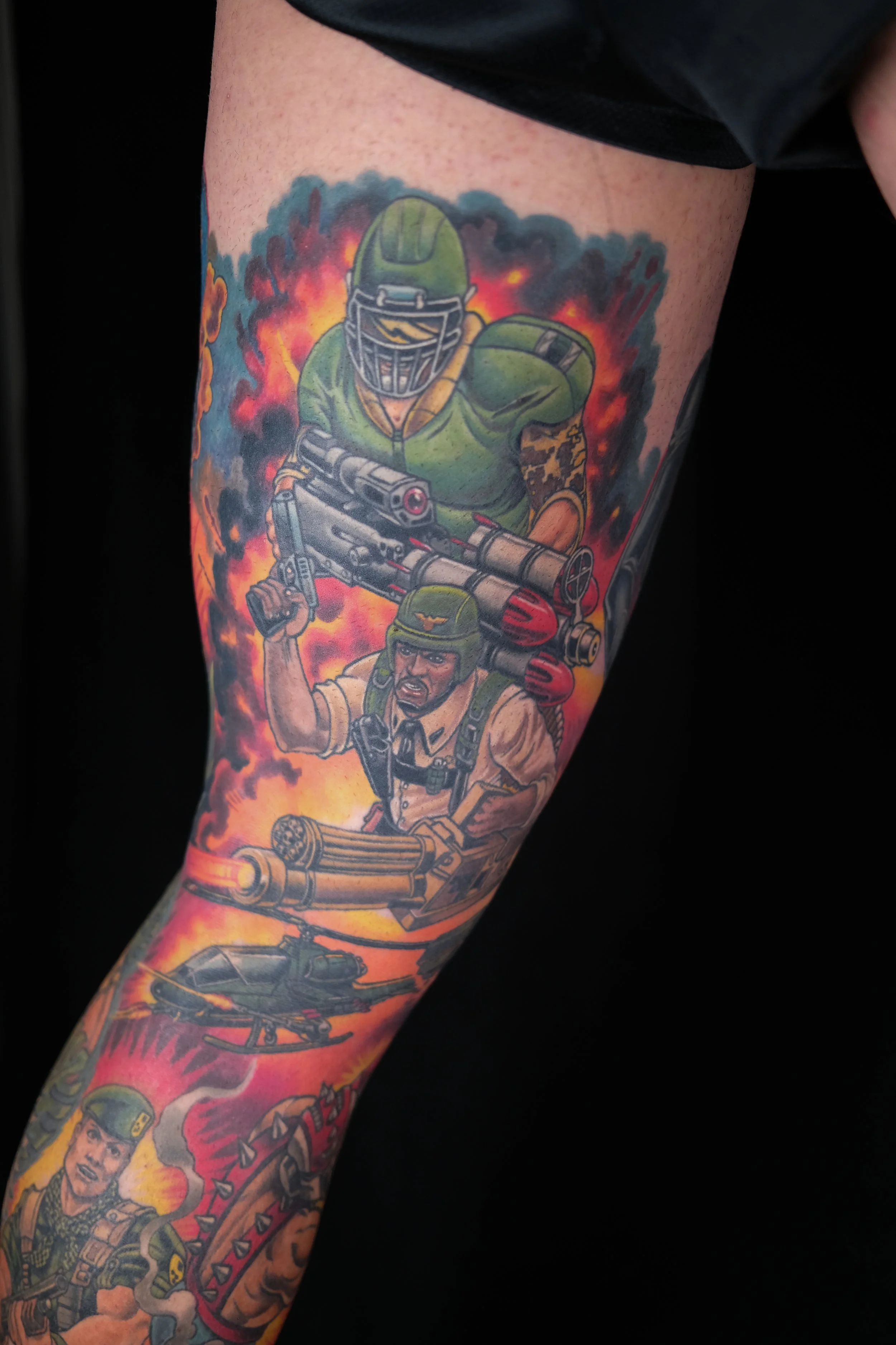 Colorful tattoo sleeve featuring a soldier with a firearm, wearing a helmet and tactical gear, with flames in the background.