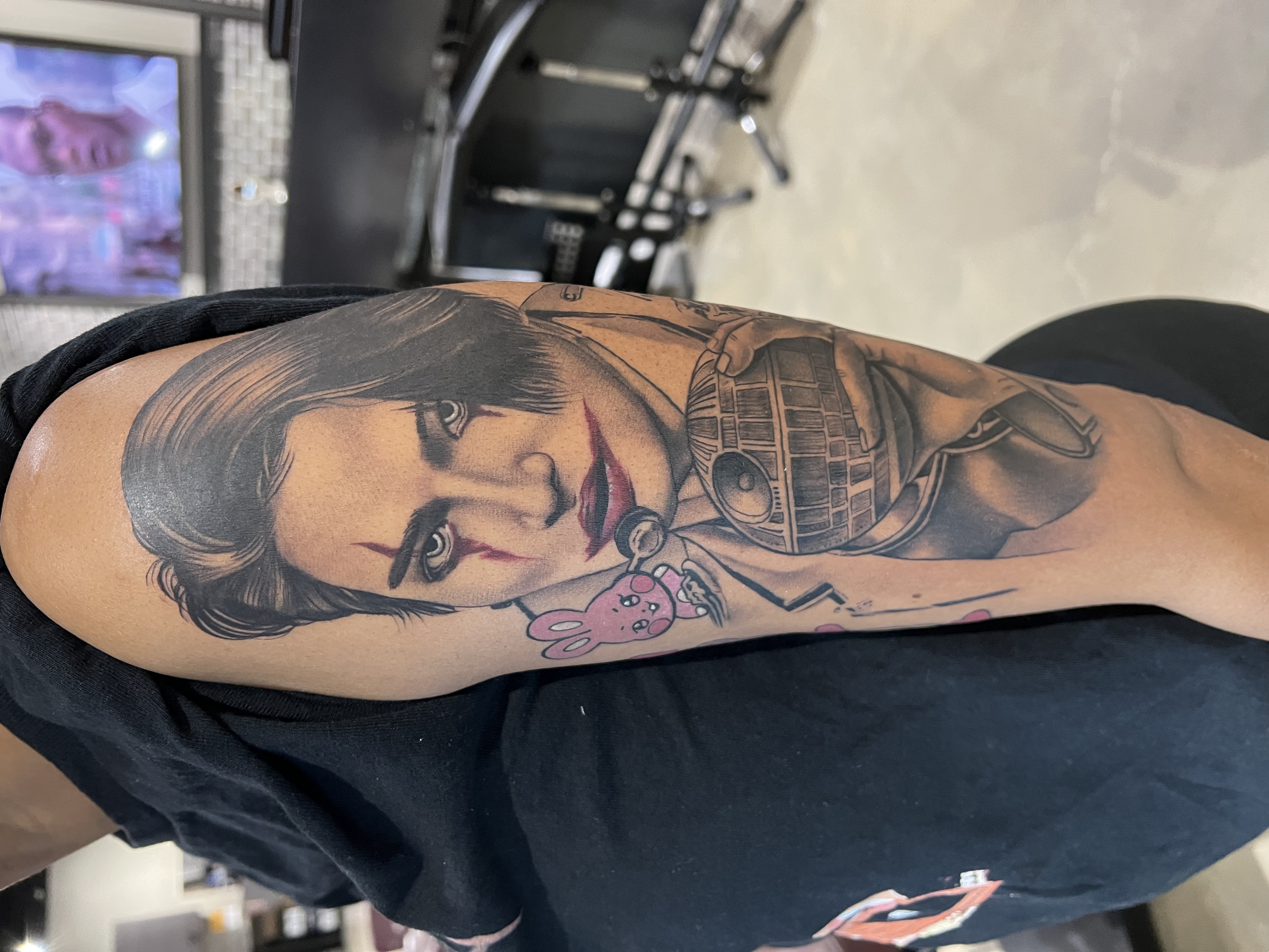 A tattoo of a woman holding a camera on a person's arm with a shopping mall or store interior in the background.