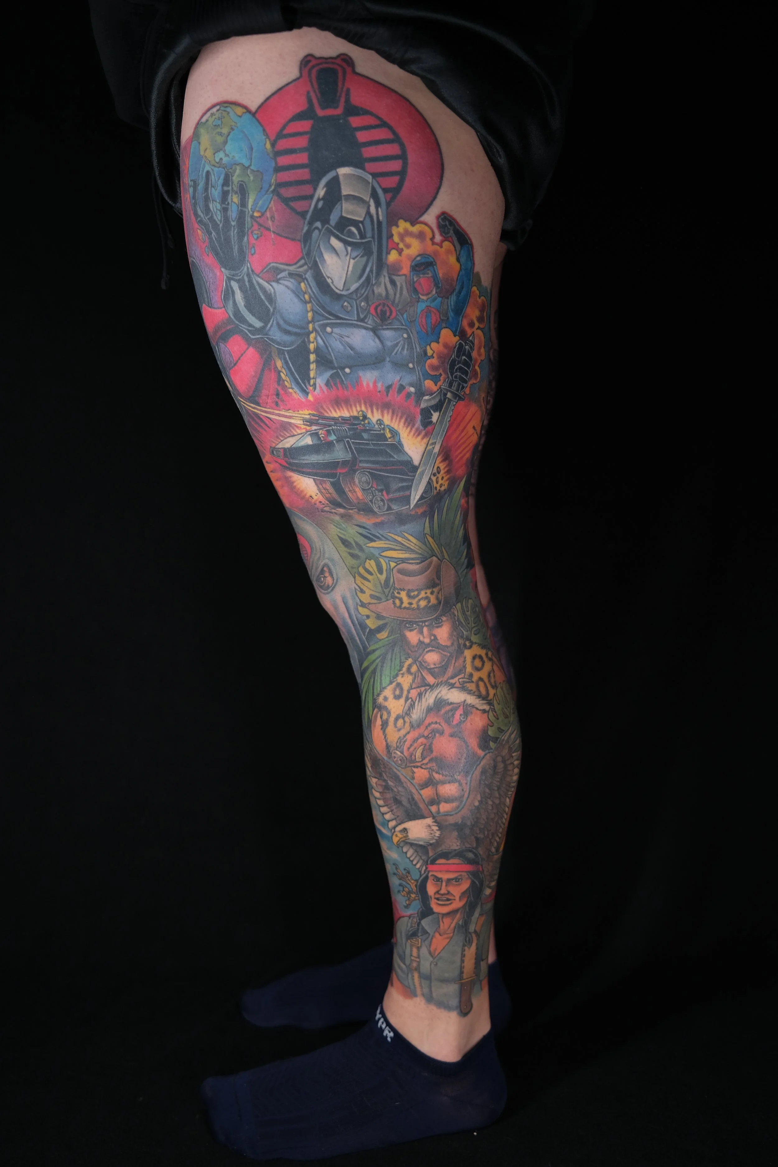 Colorful tattoo sleeve featuring a robotic character holding the Earth, a tank, a woman in military gear, and various other designs.