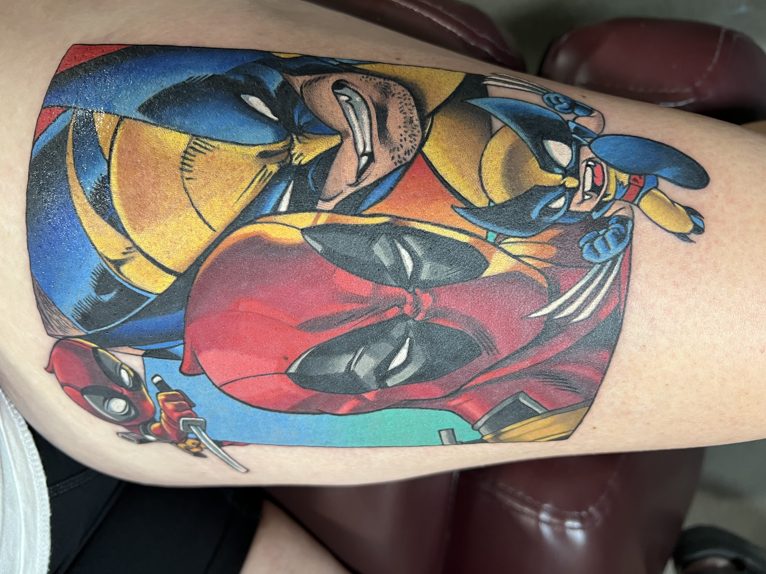 Close-up of a colorful tattoo featuring Deadpool with his arms crossed, in a comic style with bold lines and vibrant colors on person's skin.