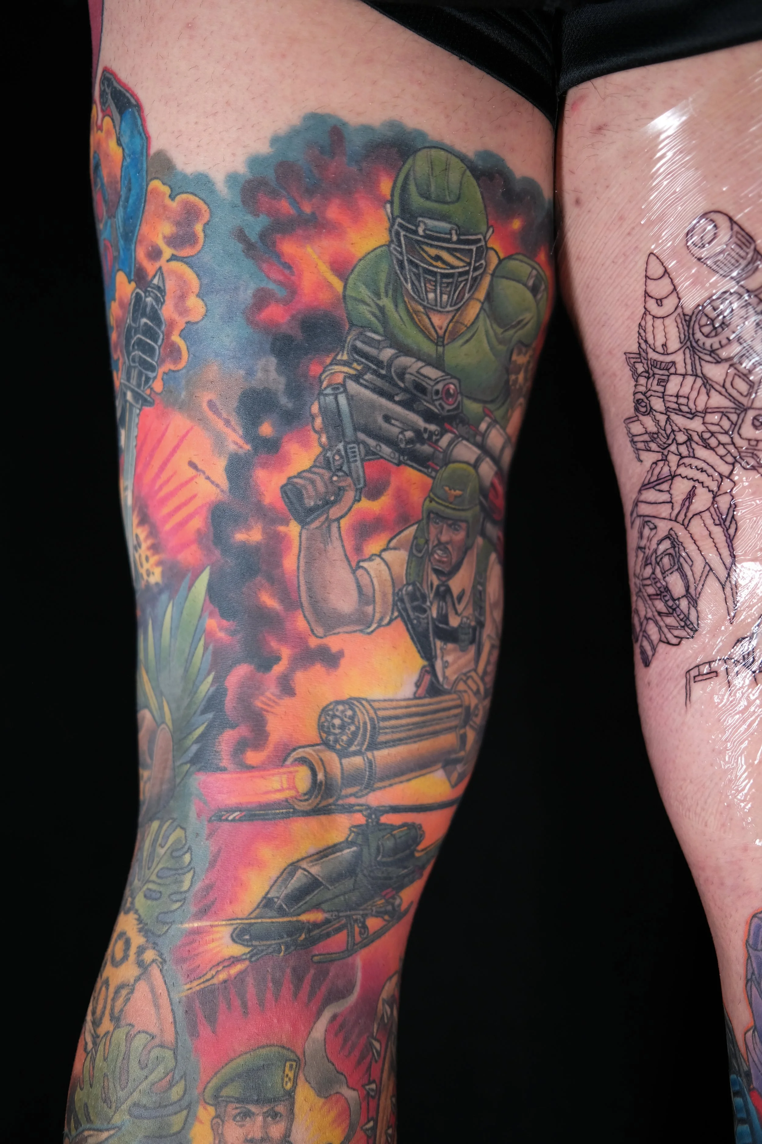 Colorful tattoo sleeve depicting a soldier in camouflage helmet and uniform, holding a large gun, with an explosion background.