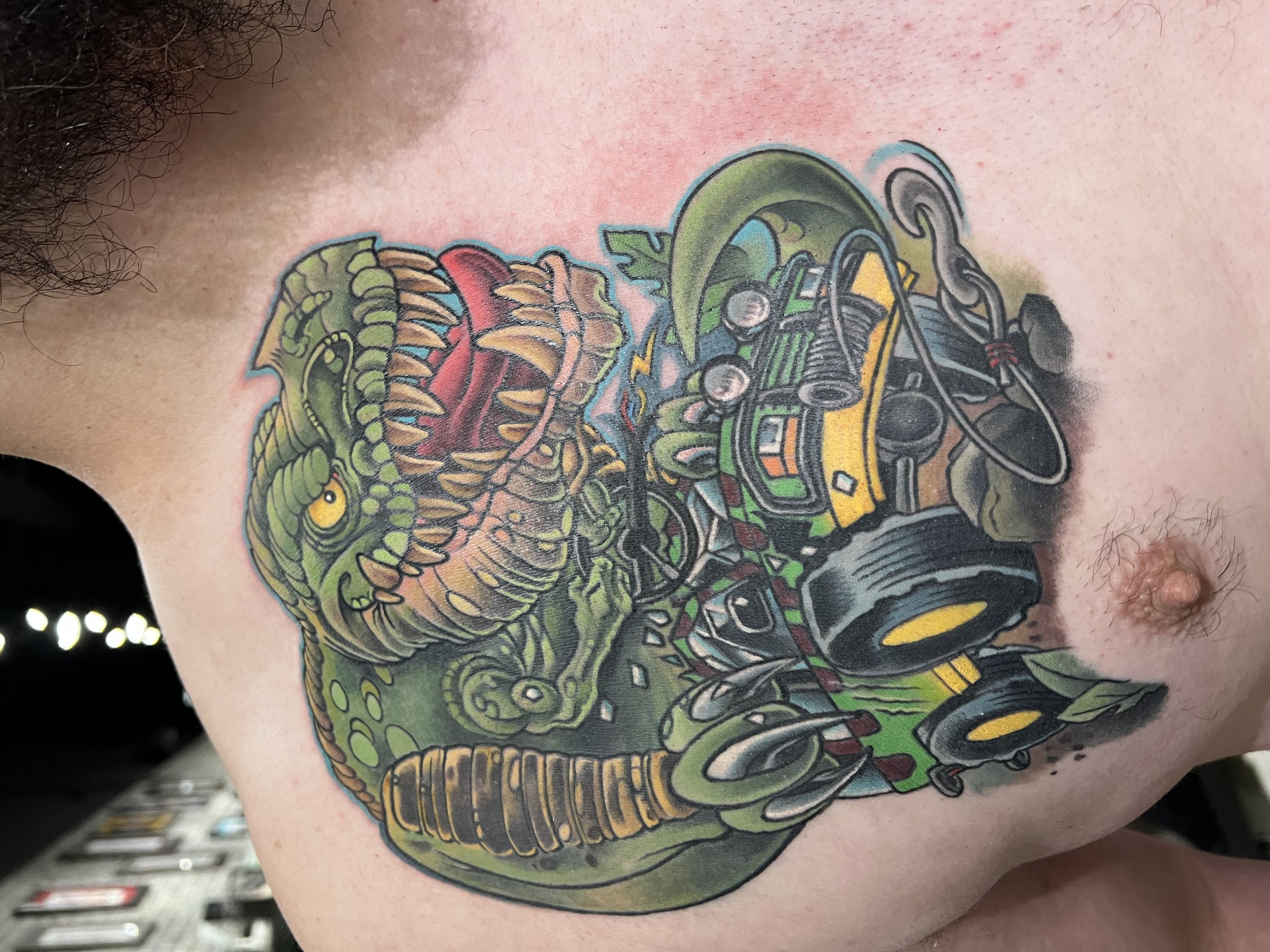 Colorful tattoo of a dinosaur on a person's shoulder, with sections of red, green, yellow, and black ink.