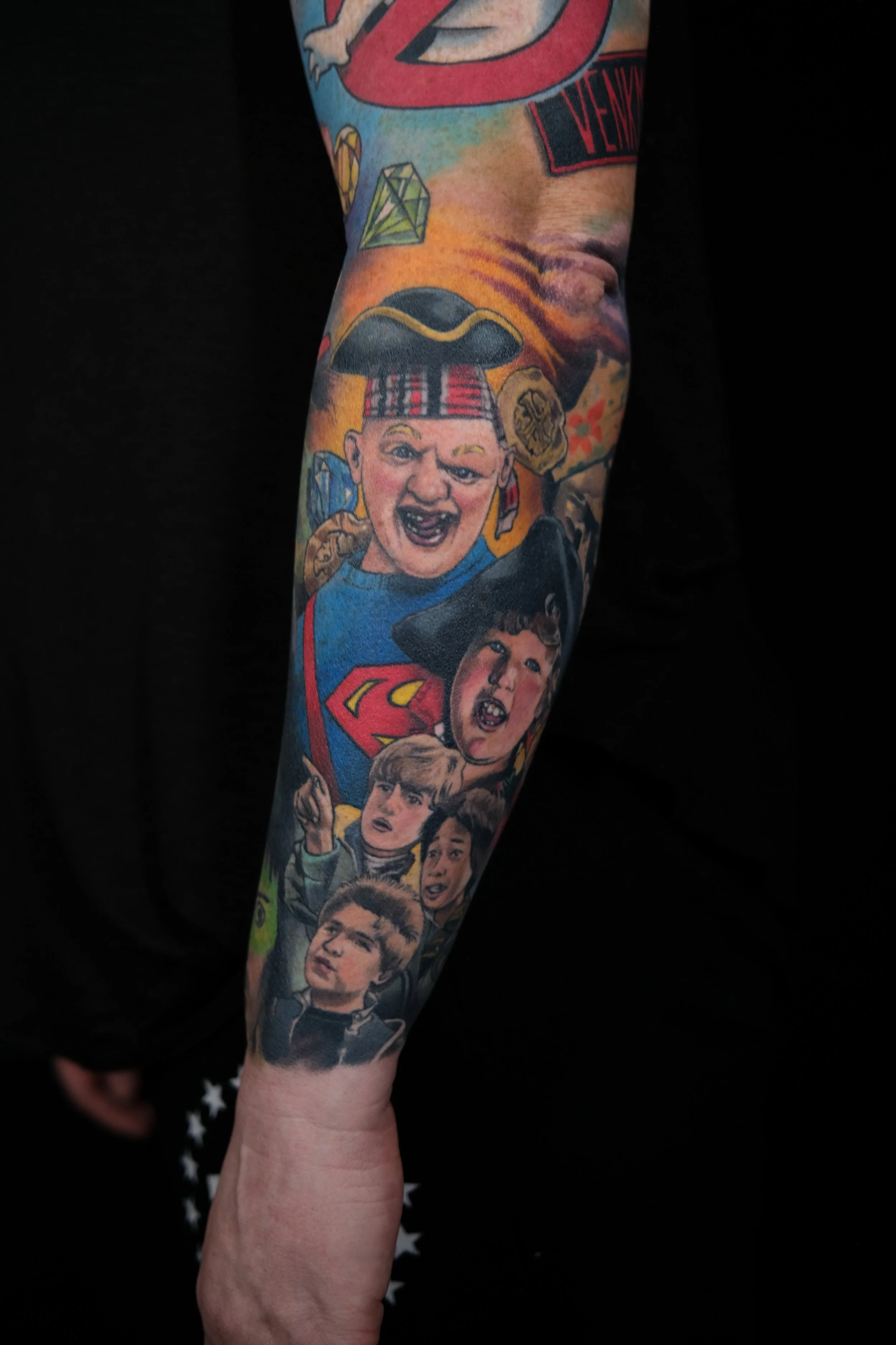 A tattoo sleeve featuring various comic book characters including Superman, a character with a zippered head, and children with expressive faces.