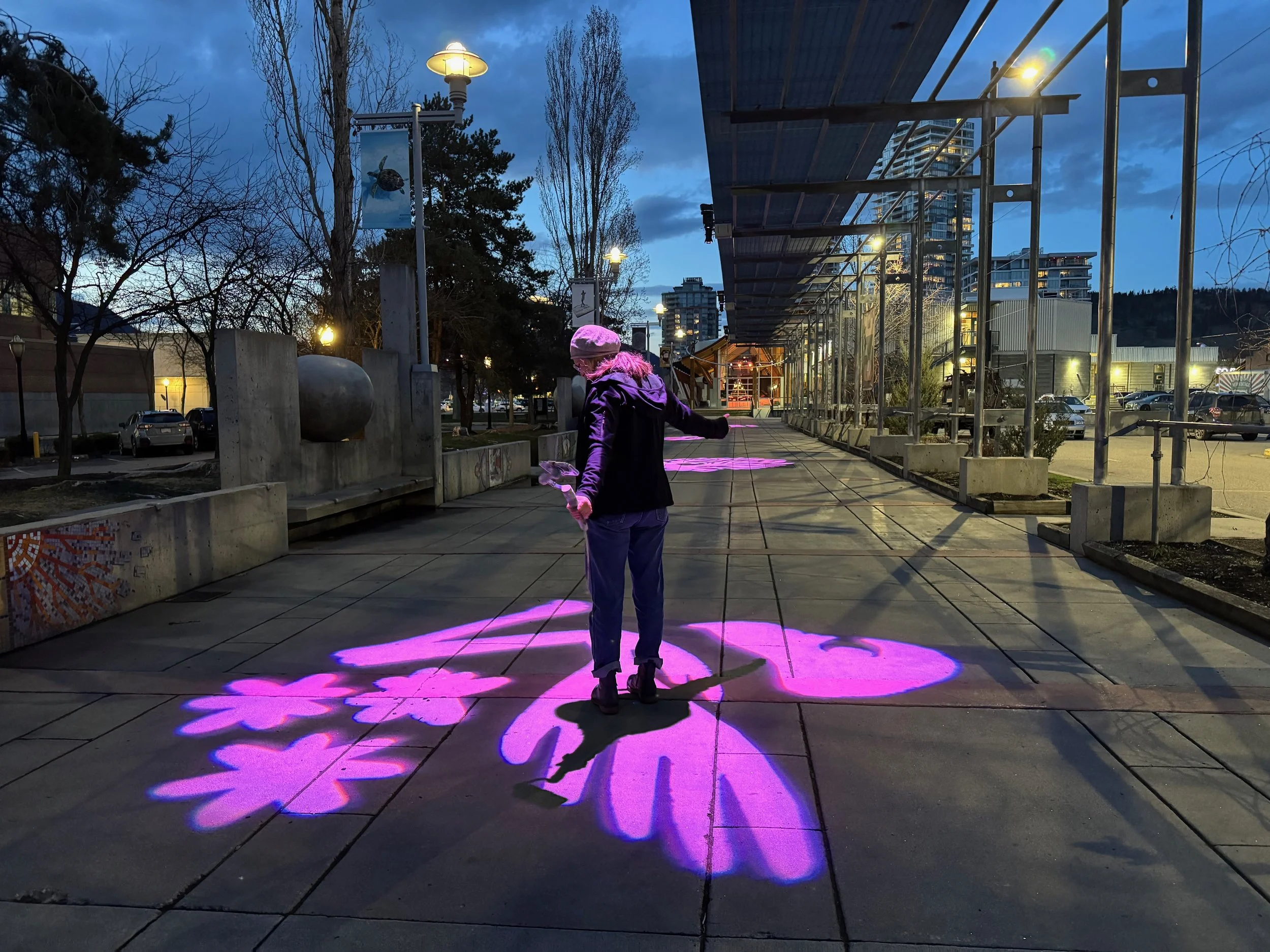 Person walking on sidewalk at dusk, illuminated by pink and purple flower-shaped light projections