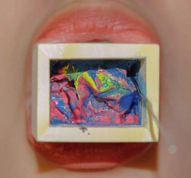 Lips holding a watercolor painting in a small, square frame.