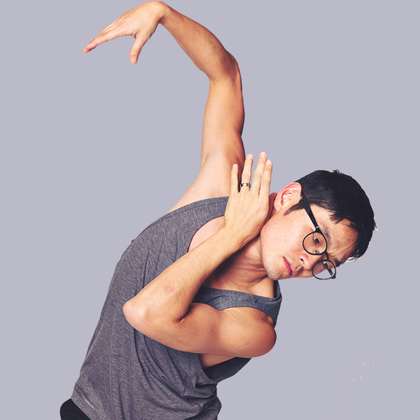 A man wearing glasses and a gray sleeveless shirt performing a stretch or yoga pose against a plain background.