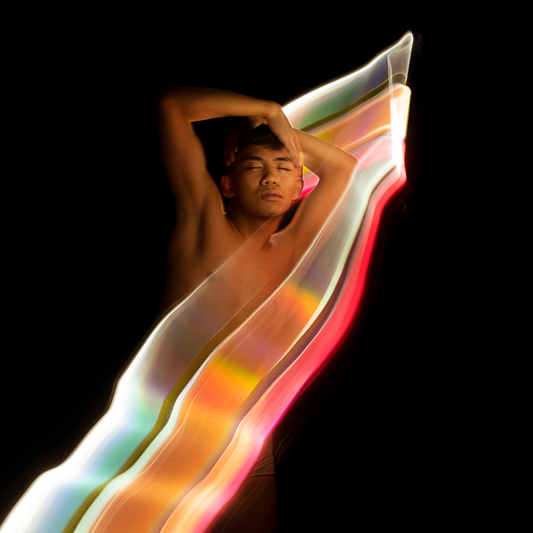A shirtless person with closed eyes, holding their head with one hand, with colorful light streaks creating a dynamic effect against a black background.