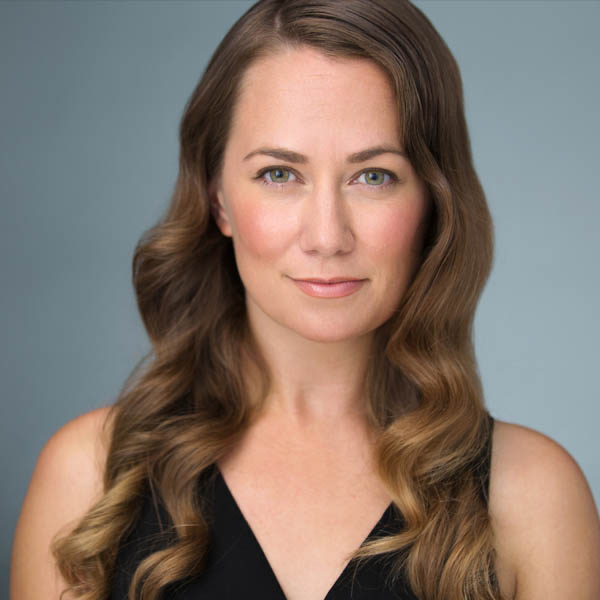 Headshot of a woman with long wavy brown hair, wearing a black sleeveless top against a plain background.