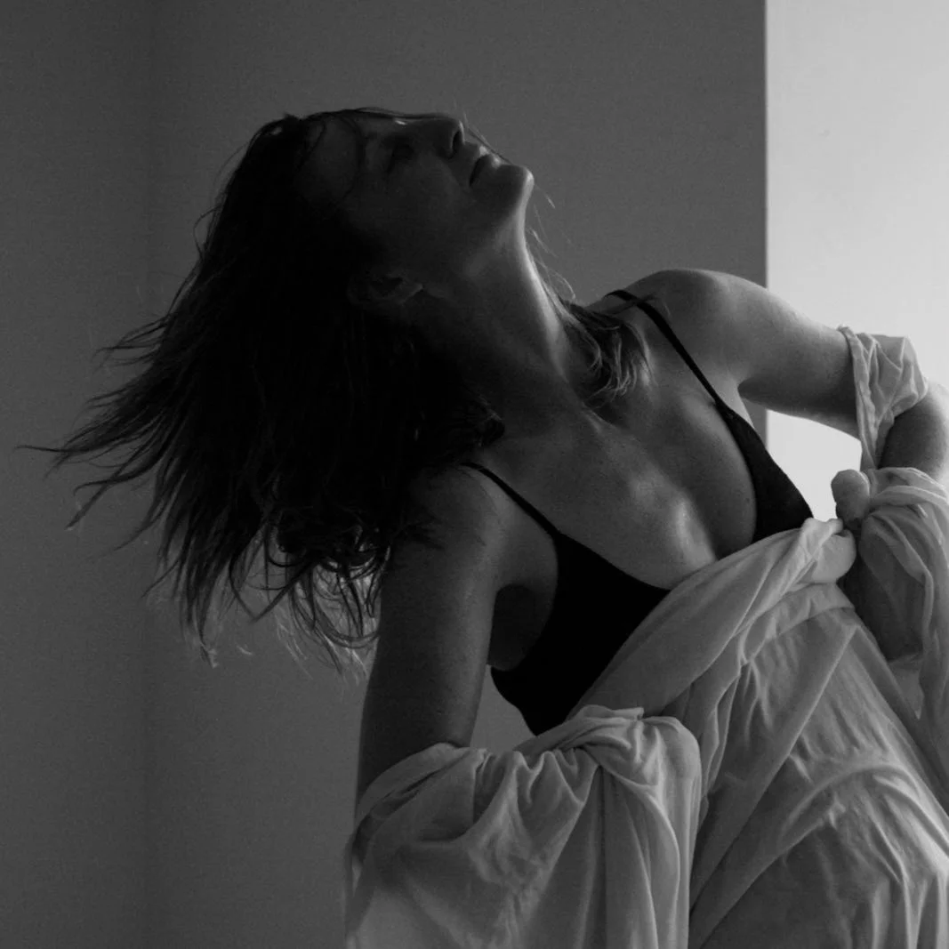 Black and white photo of a woman with wet hair, wearing a black top, leaning back and tilting her head upwards.