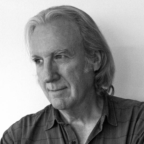 Black and white portrait of a middle-aged man with long gray hair, looking to the side with a slight smile.