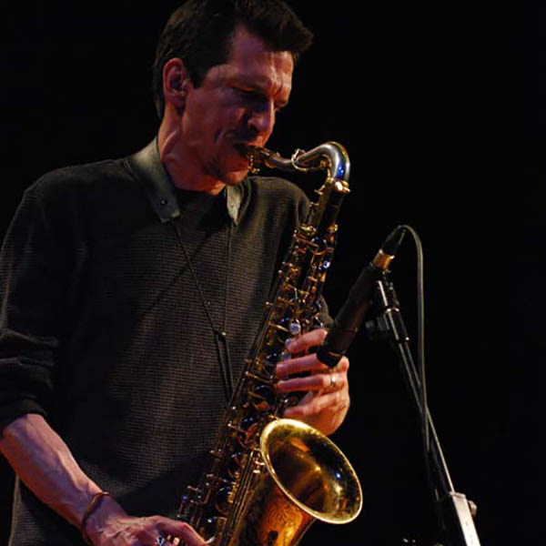 A man playing a saxophone on stage with a microphone in front of him.