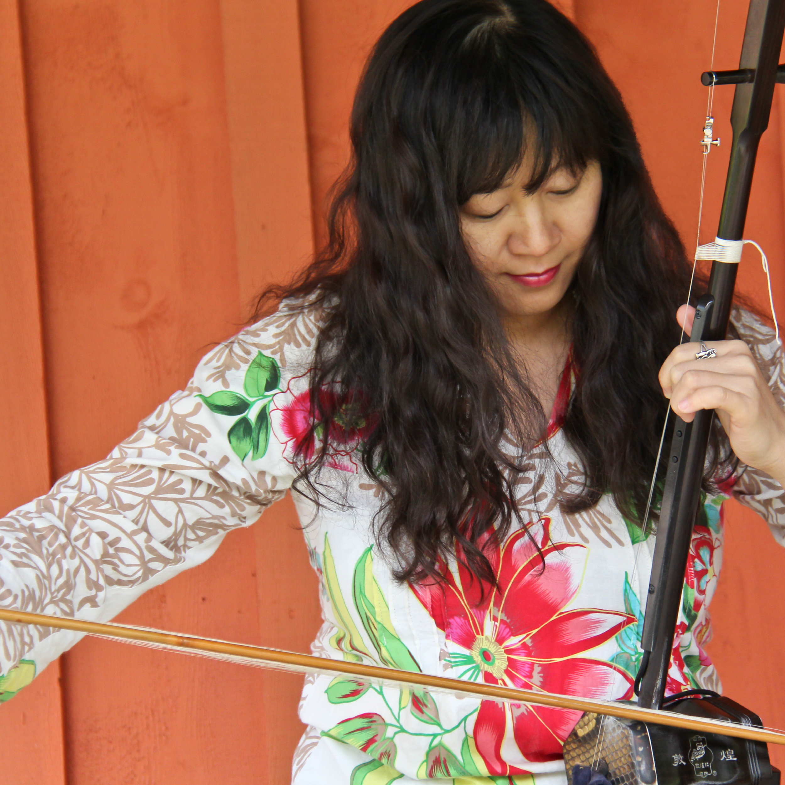 Woman playing a violin in front of a wooden background.