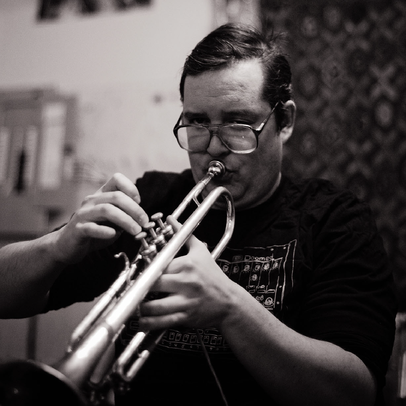 A man with glasses playing a trumpet in a room.