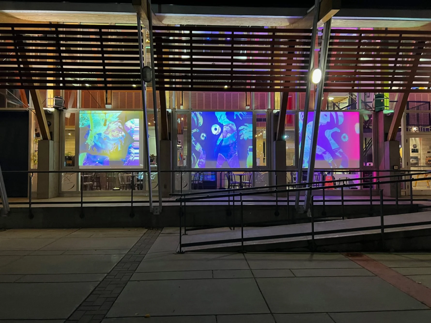 The exterior of a building at night with large windows displaying colorful, abstract digital art projections inside.