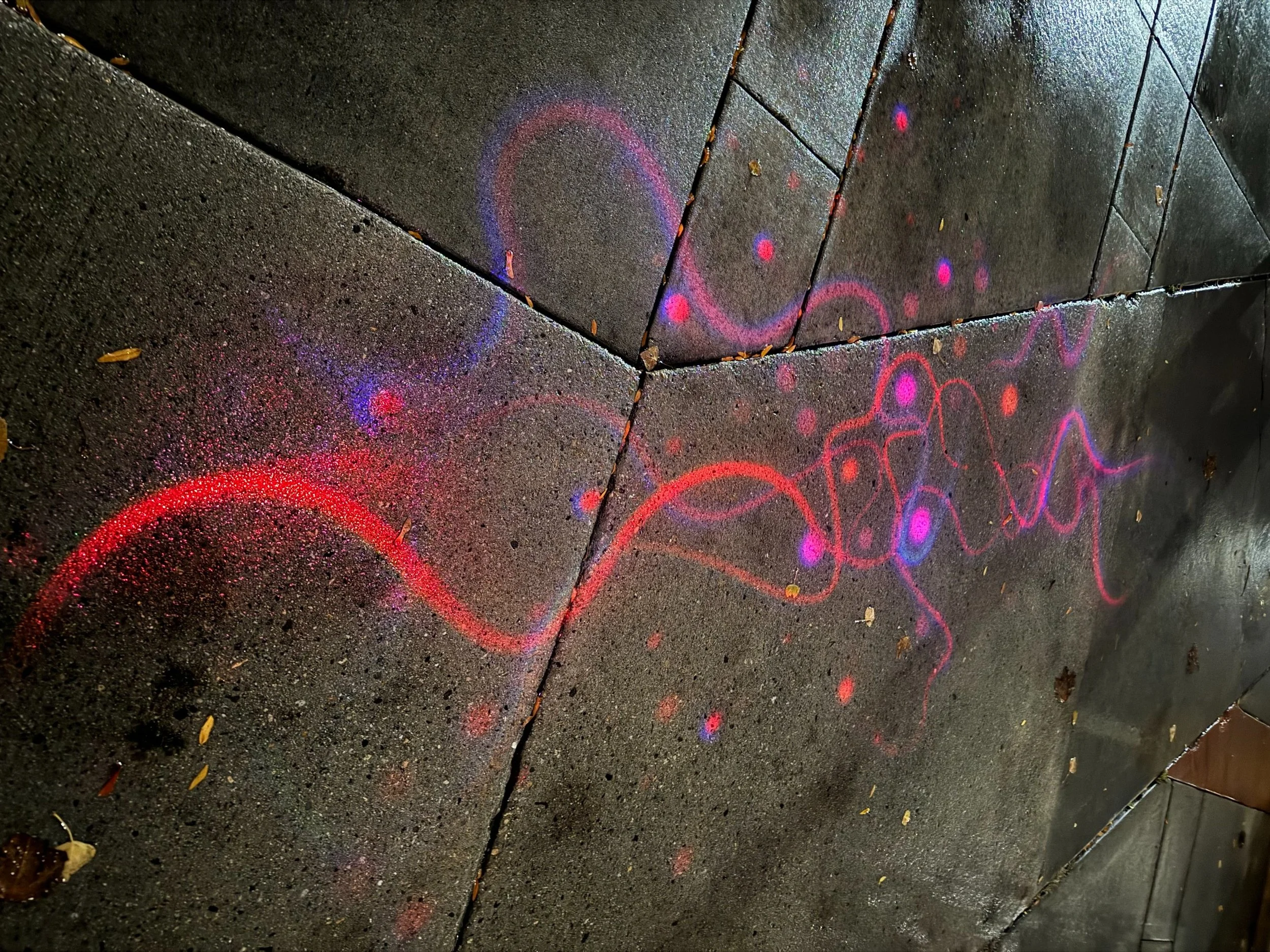 Colorful chalk art on a wet sidewalk with pink, red, and purple lines forming abstract shapes and patterns.