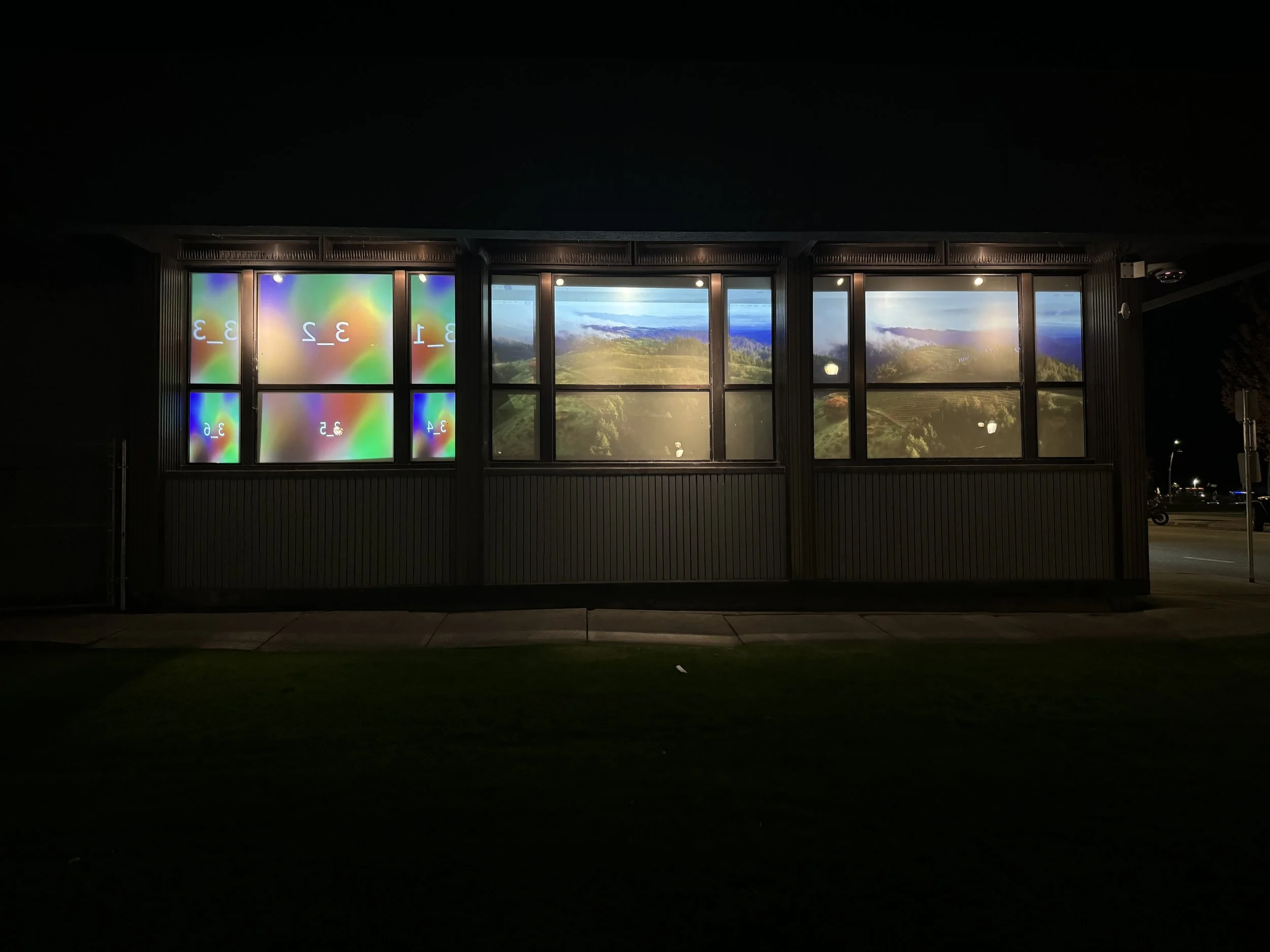 Night view of a building with large windows displaying landscape images and digital screens showing colorful, abstract patterns with numbers.